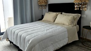 Een slaapkamer met een groot bed, grijze gordijnen, een zwart hoofdeinde en twee hanglampen.