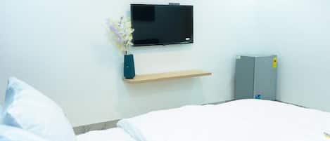Una habitación de hotel con una cama, un televisor en la pared, un estante pequeño y un armario.