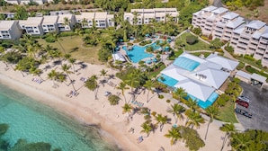 Vista aérea de un complejo turístico con una piscina grande, playa y varios edificios de hotel.