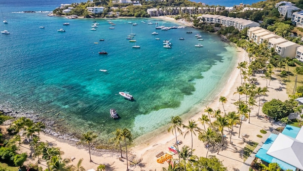 Un resort costero con aguas turquesas cristalinas, una playa de arena y una hilera de villas frente al mar.