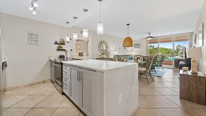 Una cocina amplia con una isla grande, elegantes lámparas colgantes y un comedor con vistas al exterior.