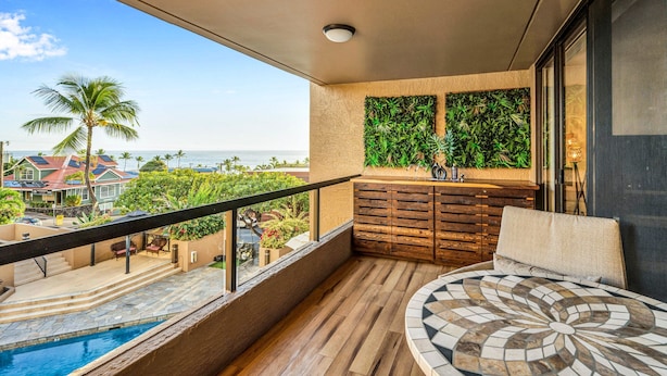 Een balkon met een zwembad, houten vloeren, een zithoek met kussens en uitzicht op de oceaan.
