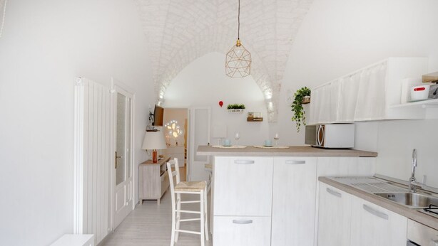 A modern kitchen with white cabinetry, a central island, and a hanging light fixture. - GuestHost - Lovely apartment equipped with every comfort for 2 people and located in a typical stone building, of which it retains striking features in the internal architecture, such as the characteristic stone vault in the living area. The flat is loca (Ostuni)