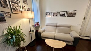 Una sala de estar con un sofá, una mesita de centro, una lámpara, una planta en maceta y cuadros en la pared.