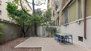 Un área de patio al aire libre con una mesa y sillas, rodeada por un muro bajo y vegetación.