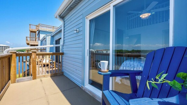 Un balcone con pavimento in legno, una sedia blu e una porta vetrata che dà su una zona piscina.