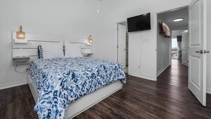 Una camera da letto con un letto, una ventola a soffitto, una TV fissata al muro e una porta che dà su un'altra stanza.