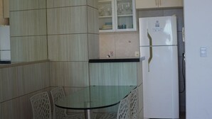Une cuisine compacte avec une table à plateau en verre, deux chaises, un réfrigérateur blanc et un meuble avec des portes en verre.