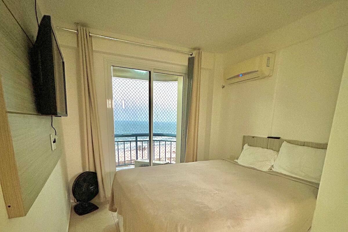 Une chambre à coucher avec un lit, une télévision et une vue sur la mer, accessible par une porte-fenêtre donnant sur un balcon.