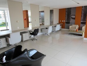 Un elegante salone moderno, ben illuminato, con un grande specchio, una poltrona da parrucchiere nera e un'area salotto con divano e tavolino.
