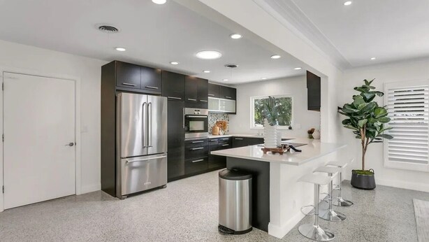 A modern kitchen with dark cabinets, stainless steel appliances, and a central island with bar stools. - Siesta Home, A Serene Retreat (Sarasota)