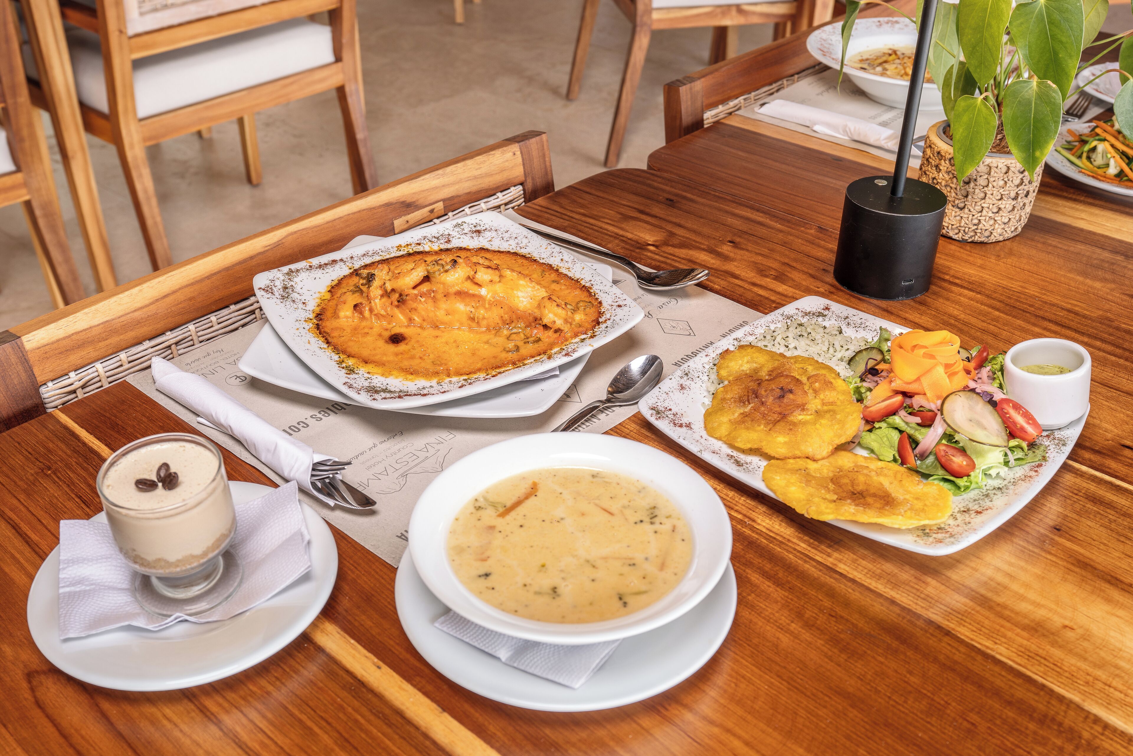 A wooden dining table with a variety of dishes including a pie, soup, and salad, along with a coffee cup.