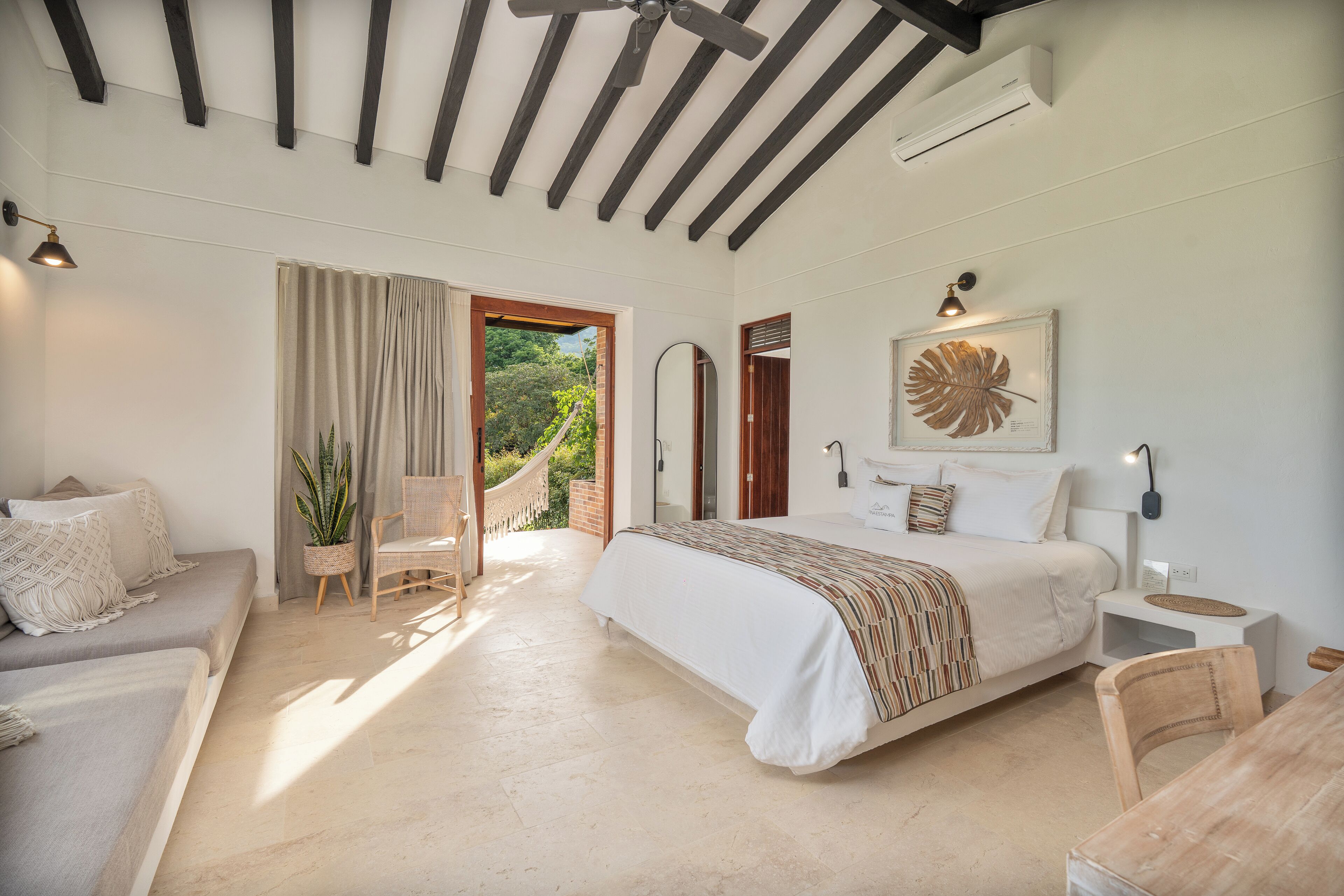 A bedroom with a large bed, a sofa, a dining table, and a ceiling fan.