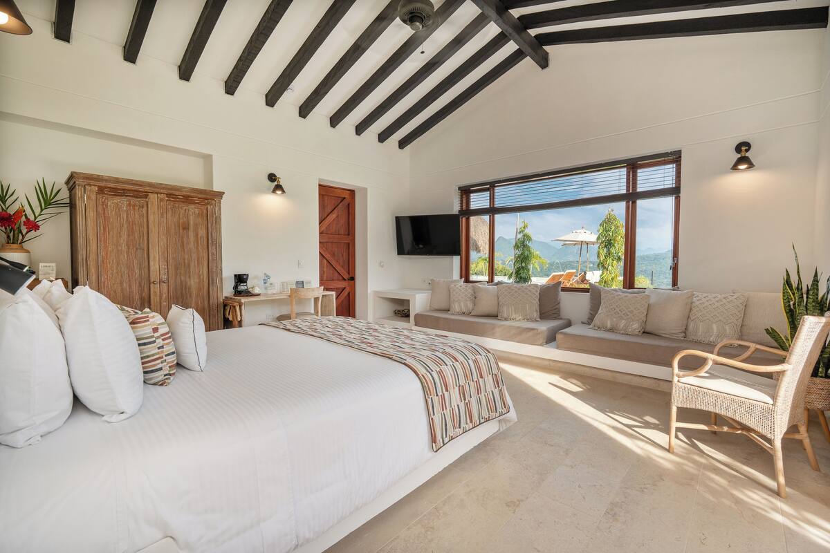 Une chambre spacieuse avec un grand lit, une armoire en bois, un canapé et un téléviseur fixé au mur.