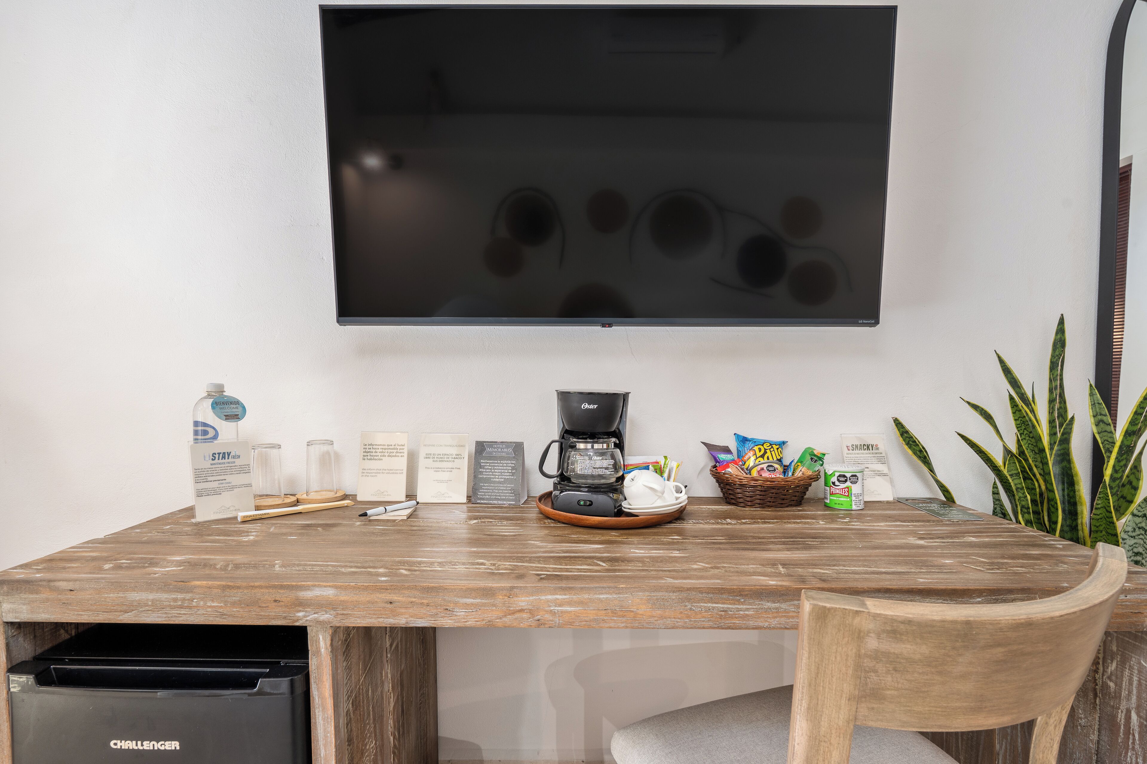 A wooden dining table with a coffee maker, snacks, and a TV mounted on the wall.