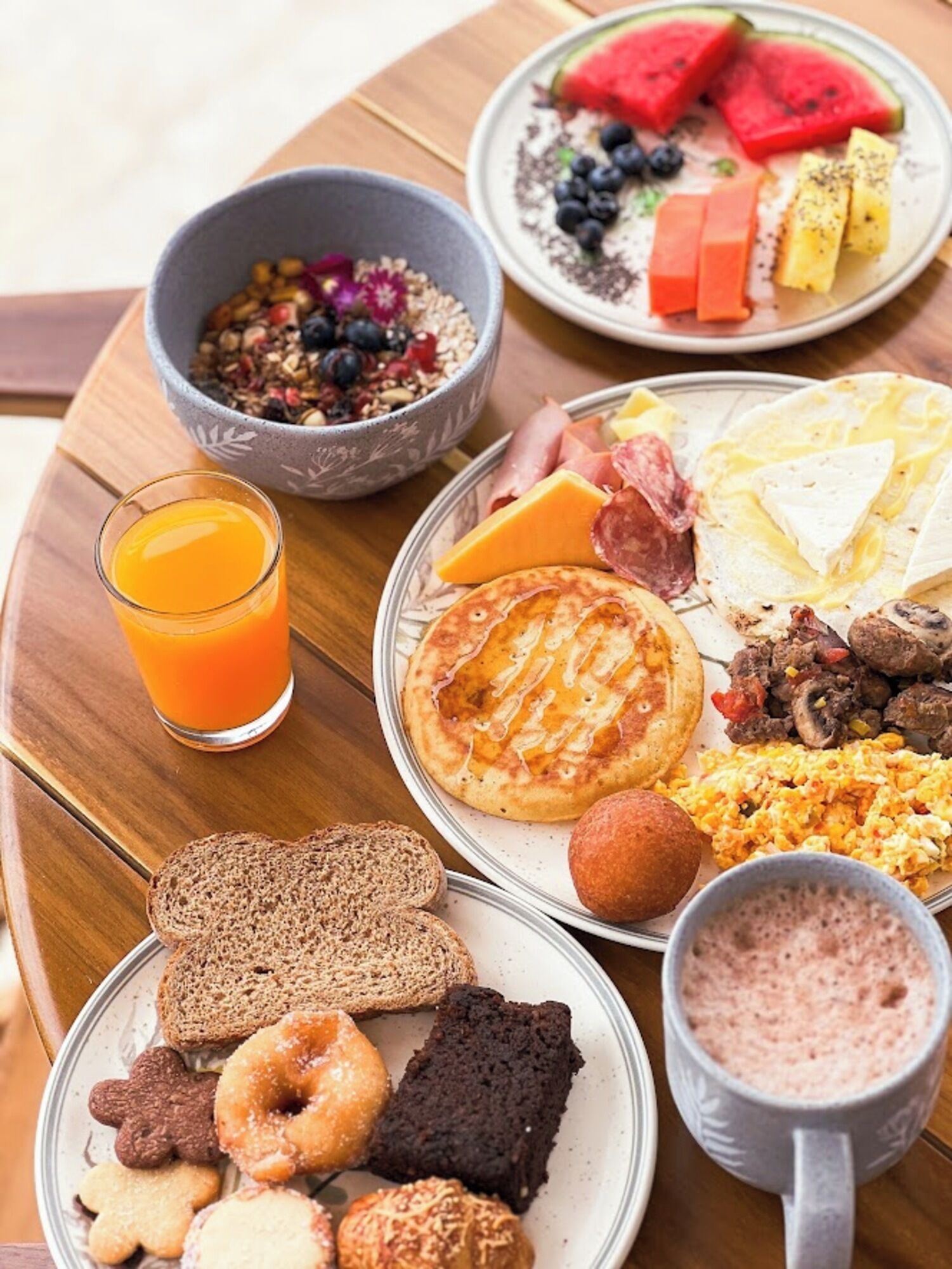Une table de petit-déjeuner avec divers plats, notamment des crêpes, des œufs brouillés, des toasts et un saladier de fruits.