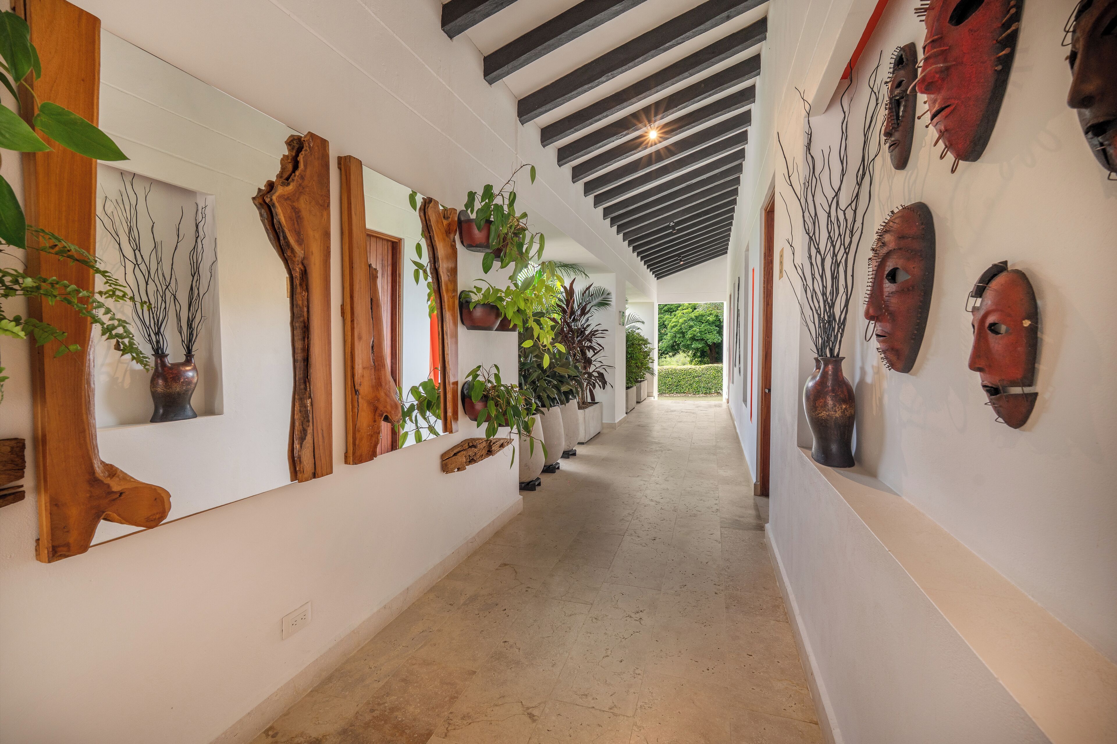 A hallway with wooden wall art, potted plants, and traditional masks on display.