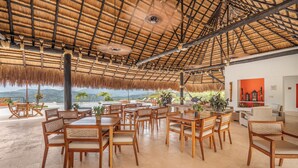 A spacious outdoor dining area with wooden tables and chairs, a thatched roof, and a view of the landscape. - Fina Estampa Country Hotel - Mayores de 10 años  (Támesis)