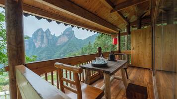 A wooden deck with a table and chairs, overlooking a mountainous landscape.
