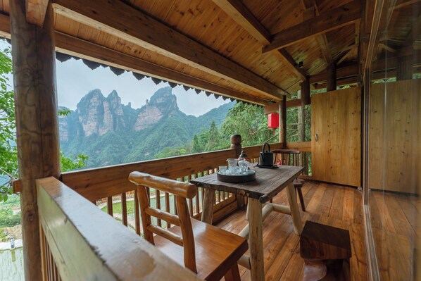 A wooden deck with a table and chairs, overlooking a mountainous landscape. - Kongjie Valley (Zhangjiajie)