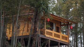 A wooden cabin with a balcony, surrounded by tall trees.