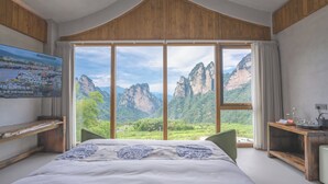 Ein Schlafzimmer mit einem großen Bett, einem Holzkopfende, einem an der Wand montierten Fernseher und Bergblick durch große Fenster.