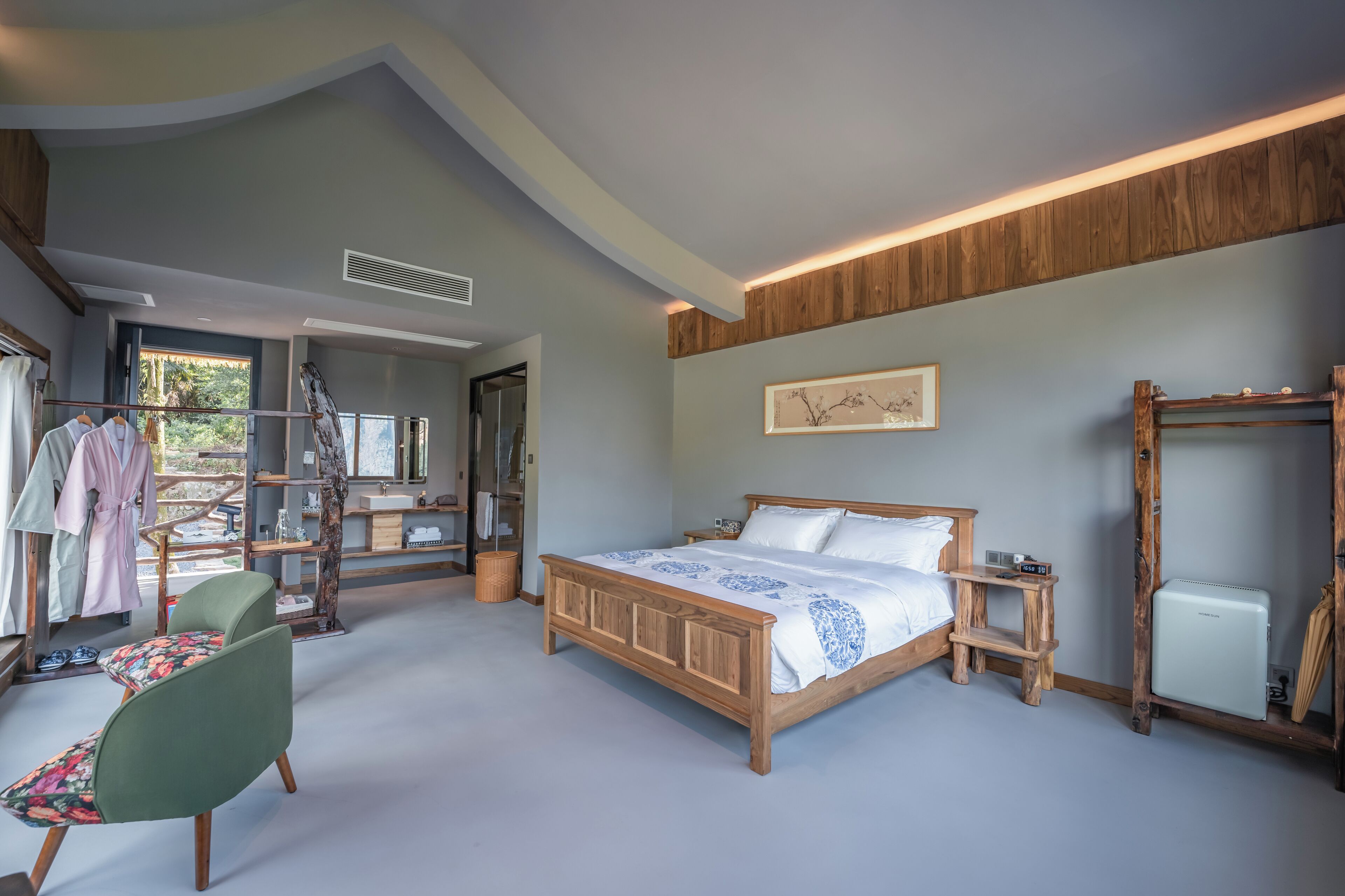 A bedroom with a wooden bed, a green chair, a wardrobe, and a window with a view.