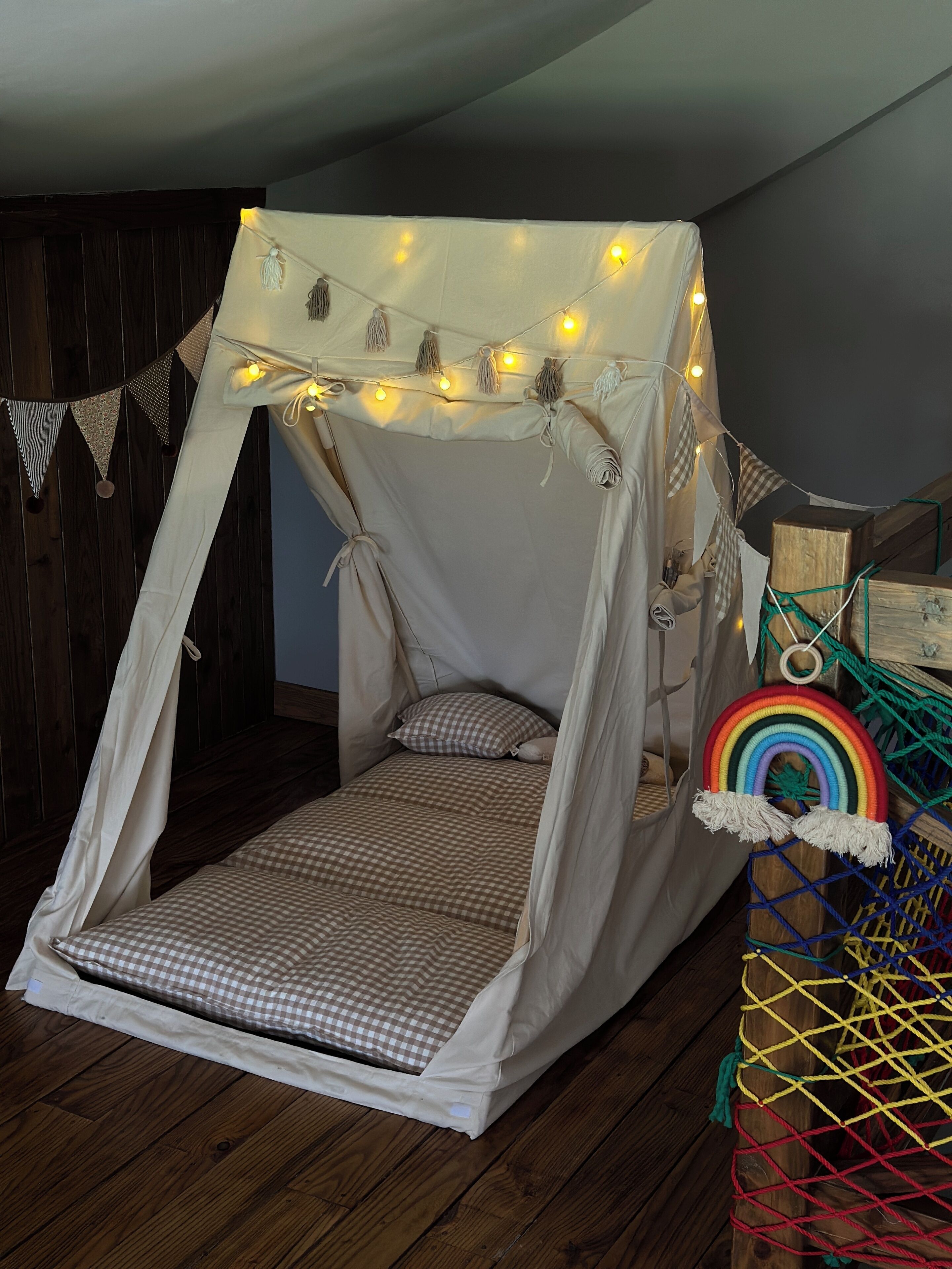 A cozy bedroom with a canopy bed, string lights, and a rainbow decoration.