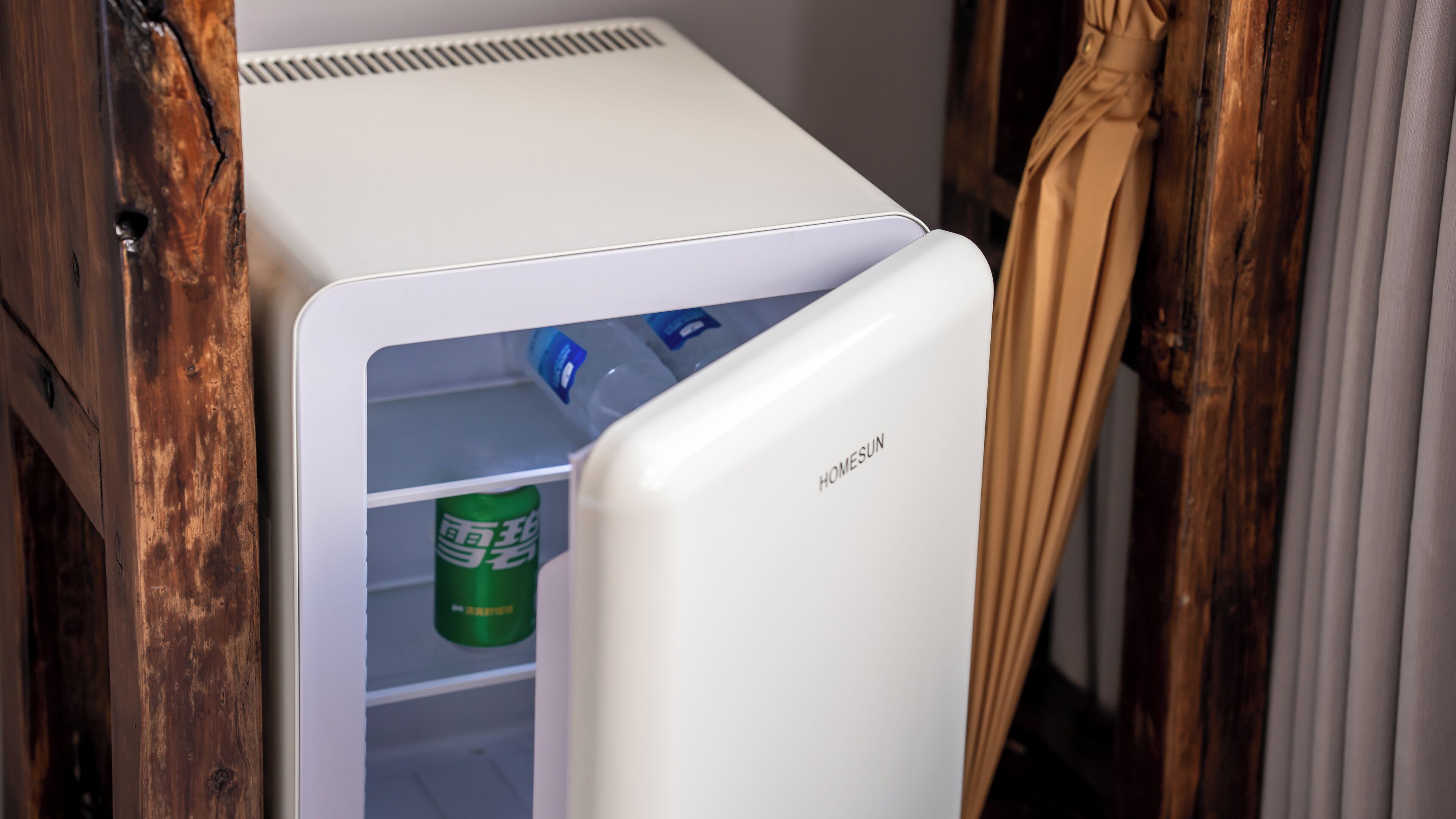 Un refrigerador blanco con el nombre de marca “HOMESUN” en la puerta, que contiene una lata verde y una botella azul.