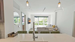 A modern kitchen with a stainless steel sink, a round mirror, and a hanging light fixture.