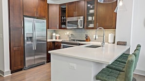 A modern kitchen with wooden cabinets, stainless steel appliances, a white countertop, and a green bar stool.