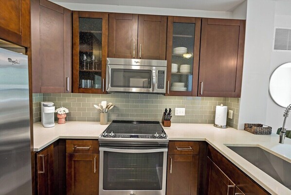 A kitchen with dark wooden cabinets, a stainless steel microwave, a built-in oven, and a white countertop.