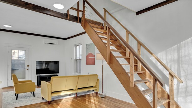 Un salon moderne avec un escalier en bois, un canapé jaune et un téléviseur à écran plat.