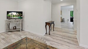 A spacious living room with a television on a wooden stand, a small table, and a wicker chair. The room has white walls and wooden flooring. - 3 Bd 2 1/2 bath Chic Large.30mto DC, 12min to IDA (Herndon)