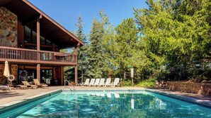 Un espace piscine avec des chaises longues, un bâtiment en pierre et des arbres environnants.