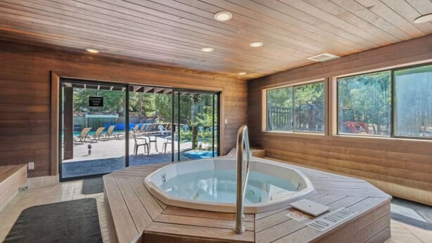 Un intérieur en bois avec un jacuzzi, une porte vitrée donnant sur l’extérieur et une vue sur l’espace piscine.