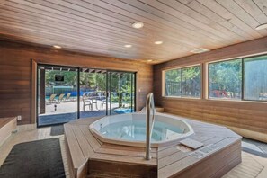 Un intérieur en bois avec un jacuzzi, une porte vitrée donnant sur l’extérieur et une vue sur l’espace piscine.
