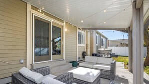 Une terrasse extérieure aménagée avec des meubles en osier, un barbecue et des guirlandes lumineuses.