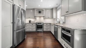 Une cuisine moderne dotée d’appareils électroménagers en acier inoxydable, de meubles blancs et d’un parquet en bois disposé en motif chevron.