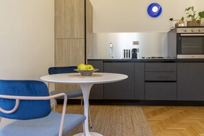 A modern kitchen with a white table and blue chairs, a bowl of fruit, and a blue wall decoration.