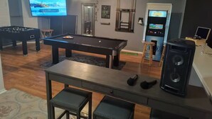 A living room with a pool table, a foosball table, a television, and a sound system.
