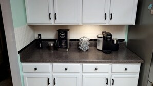A kitchen with white cabinets, a granite countertop, a coffee maker, a kettle, and a refrigerator.