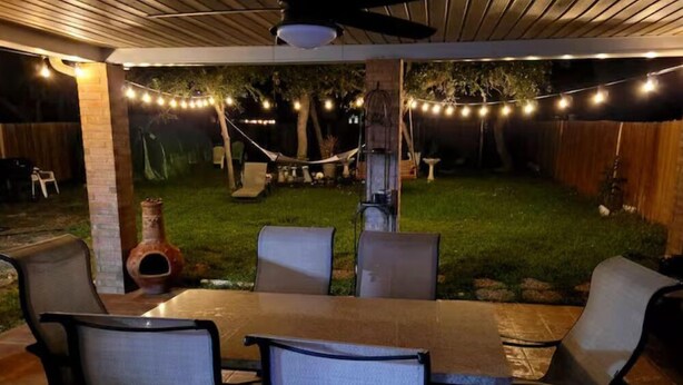 An outdoor patio with a table and chairs, string lights, and a hammock.
