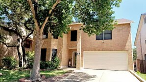 A two-story brick house with a garage, a tree in the front yard, and a clear sky.