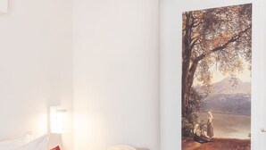 Et værelse med et stort landskabsmaleri, en rød pude og en hvid lampe.