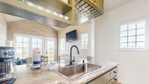 A modern kitchen with a large sink, granite countertop, and wooden ceiling beams.
