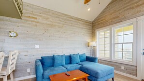 A living room with a blue sectional sofa, a wooden coffee table, and a window with a view.