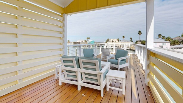 A wooden deck with white furniture and a view of the ocean.