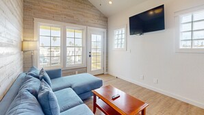 A living room with a wooden ceiling, a large TV, and a sofa.