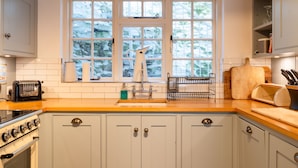 Une cuisine équipée d’un évier à deux bacs, d’une cuisinière et d’une fenêtre donnant sur les arbres.